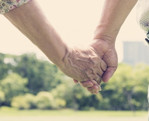 A close up of an older couple holding hands in a park