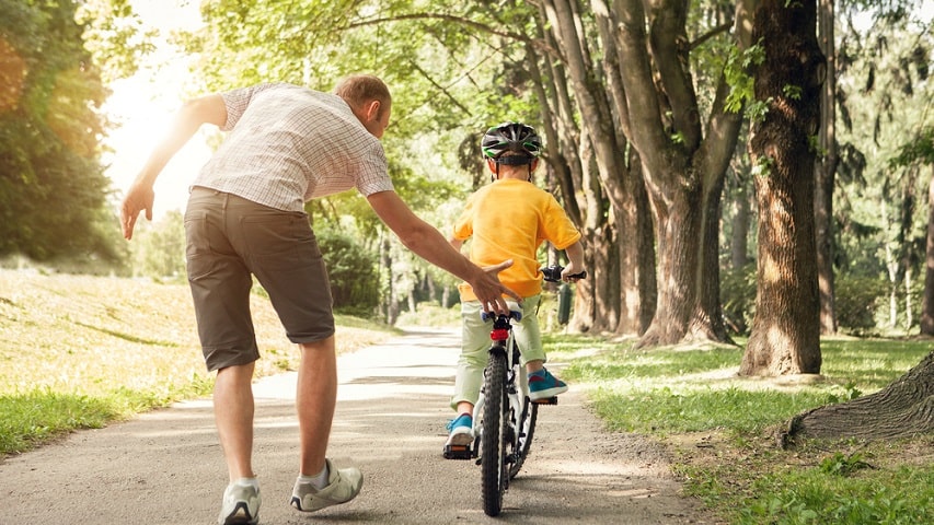 father teaching son to ride bike